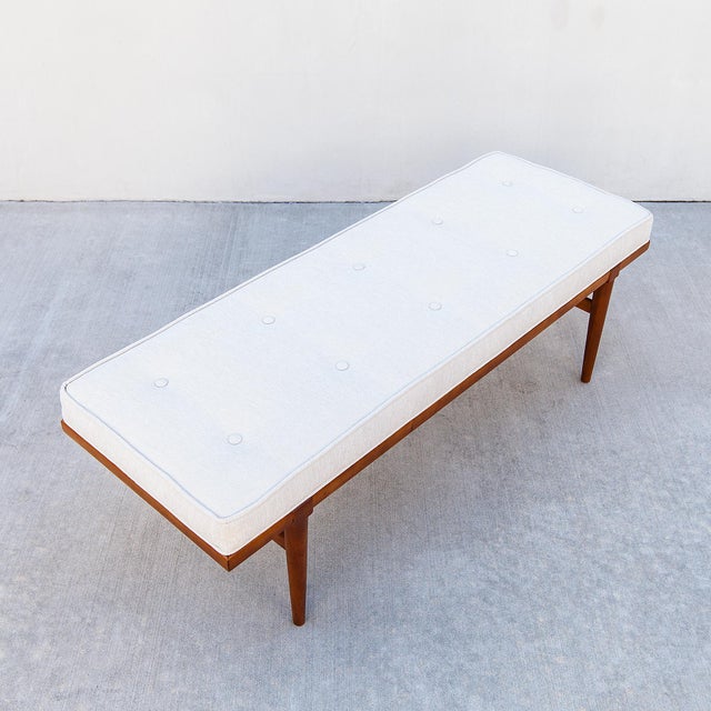 A restored entryway or bed-end bench in solid ash wood with tufted velvet upholstery, made in the United States c. 1960s....