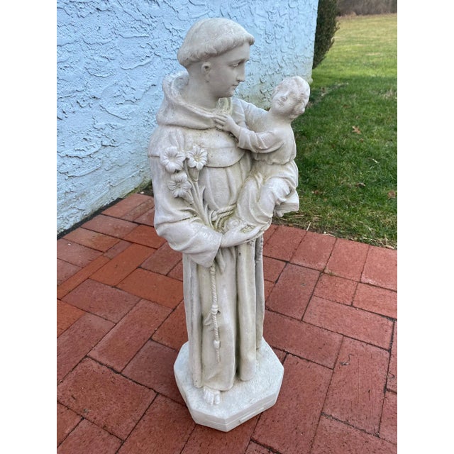 Lovely cement sculpture of St. Anthony draped in a monk's robe and holding a baby in his arms.