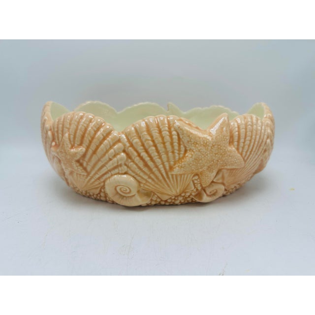 This is a small, glossy ceramic bowl with a coastal theme. It has a scalloped rim and is decorated in relief with...