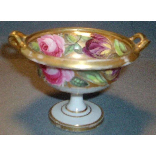 A diminutive porcelain urn highly gilt throughout with goat head handles and floral bands inside and out. Painted with...
