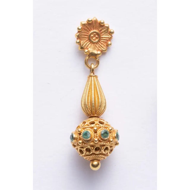 Pair of finely tooled 22K gold Indian dangle earrings with faceted round emeralds around the ball portion. A floral motif...