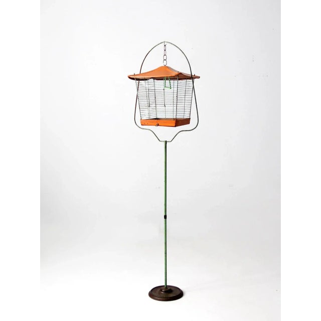 Here is a mid-century bird cage with stand. The metal cage features an orange peaked roof, with slender bars and an orange...