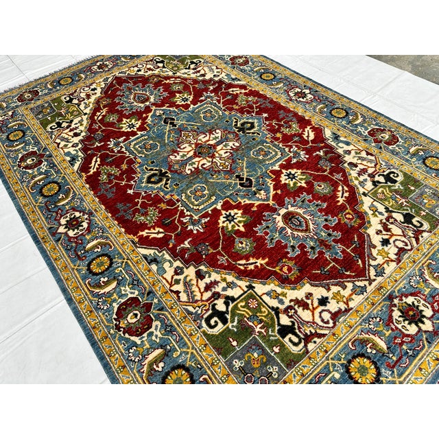 This hand-knotted Heriz rug features a bold stepped diamond medallion in deep red and slate blue, set against an ivory...