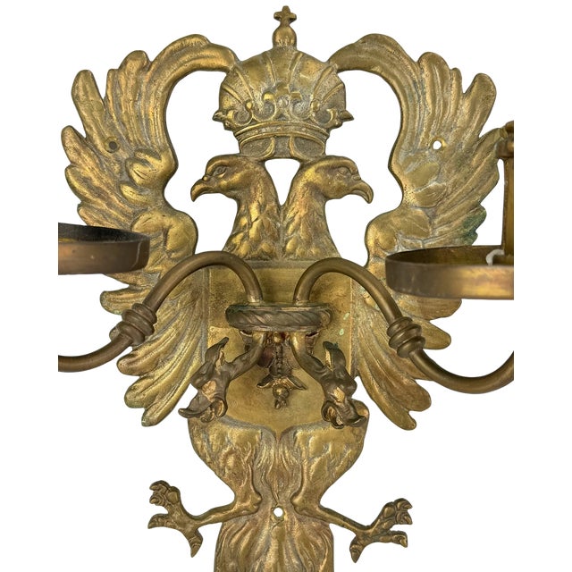 A commanding pair of Continental-style cast-brass candle sconces, combining crowned double-headed eagles, sculptural...