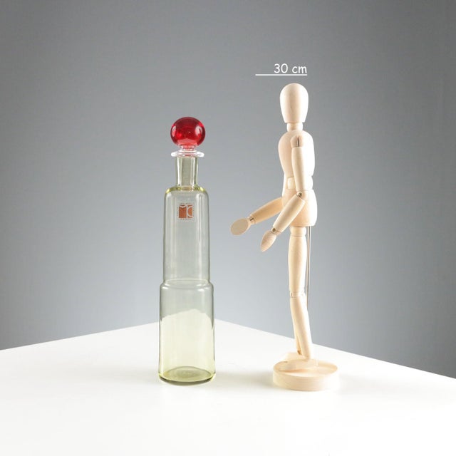 Yellow glass bottle with red cap. Designer's signature and manufacturer's sticker. Bottle height 29.5 cm. Original box....