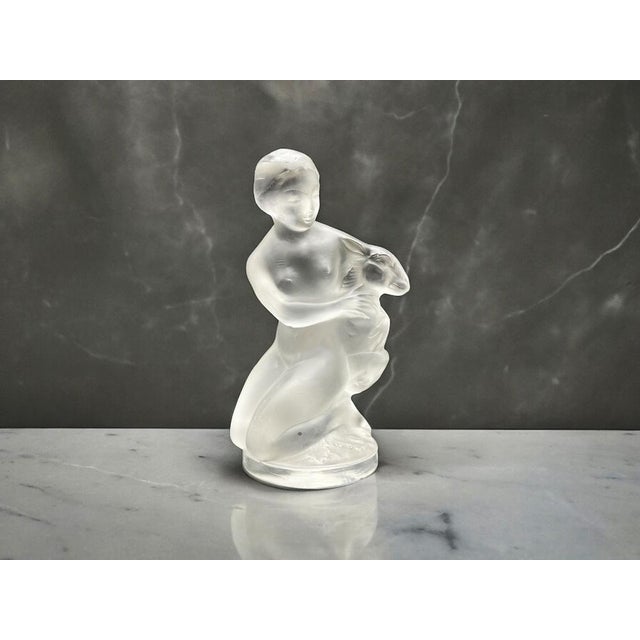 The Lalique figurine is a refined example of artistry and craftsmanship. It depicts a nude female figure with a frosted...