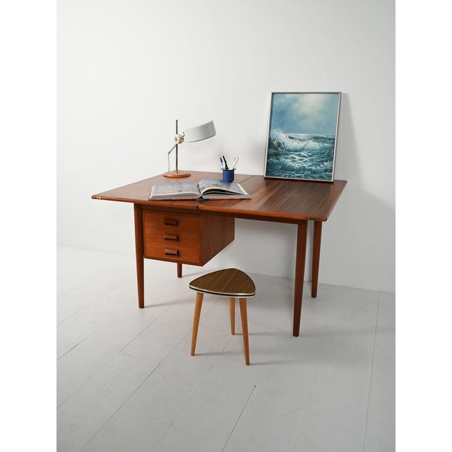 1950s/1960s teak desk with a flip-top, rotating top, a block of three suspended drawers, carved handles, and tapered...