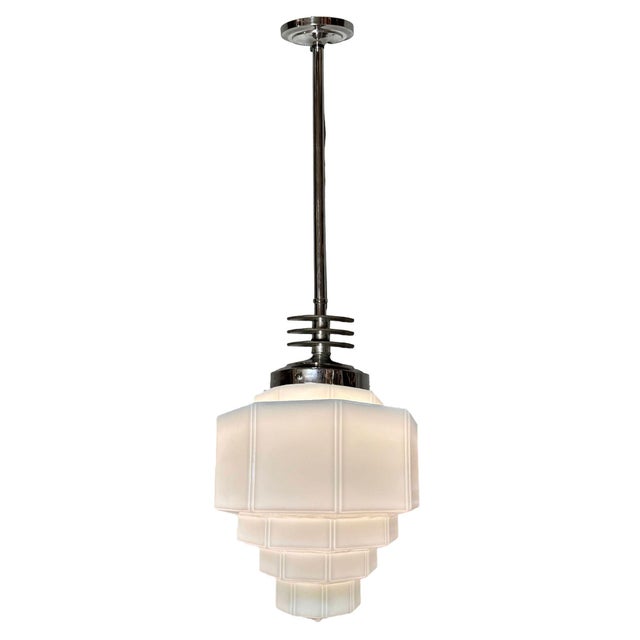 1930s Art Deco pendant light featuring a stepped milk glass shade. It is paired with a Streamline Art Deco pendant lamp...