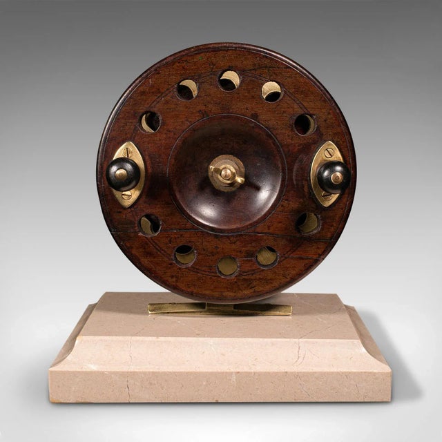 This is an antique mounted fishing reel. An English, mahogany and brass reel of sporting decorative interest and mounted...