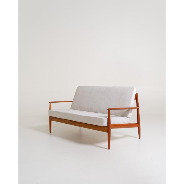Teak sofa with removable cushions, recently reupholstered in a light cotton blend. Frame with distinctive metal back...