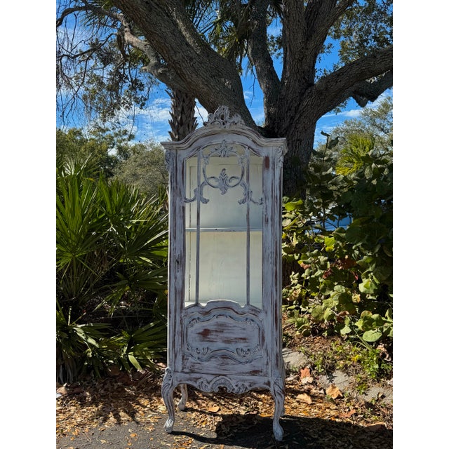 Elegant French Louis XV–style vitrine display cabinet finished in a beautifully distressed white. This tall, narrow...
