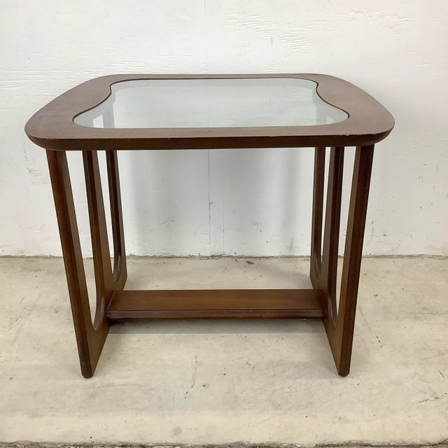 Simple yet stylish mid-century modern side table features a striking sculptural wood base with a rounded edge glass top....