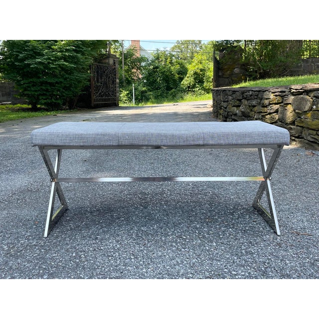 A minimalist mid-20th century modernist style bench with gray linen padded upholstery seat and cross trestle chrome base....
