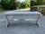 A minimalist mid-20th century modernist style bench with gray linen padded upholstery seat and cross trestle chrome base....