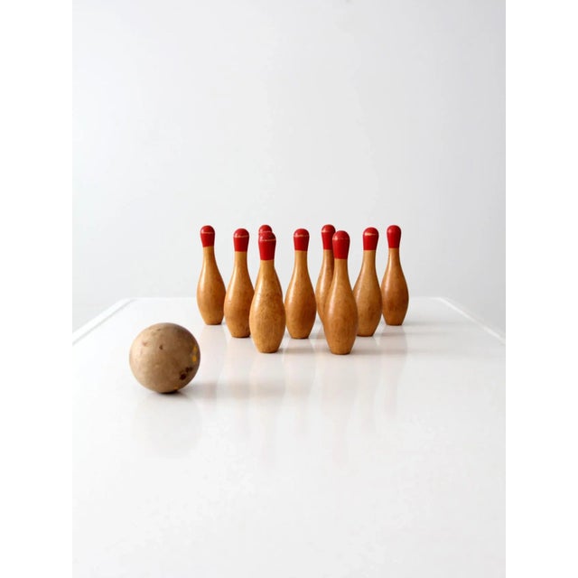 This antique table bowling set features nine wooden skittles with red painted tops and a small wooden ball with remnants...
