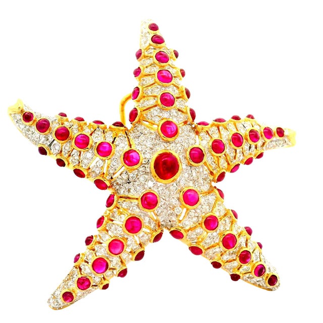 A striking brooch meticulously crafted in the shape of a starfish, adorned with cabochon-cut red rubies. The arms and...