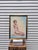 This framed artwork is a figurative piece depicting a seated female nude, signed by the Italian artist Marcello Cassinari...