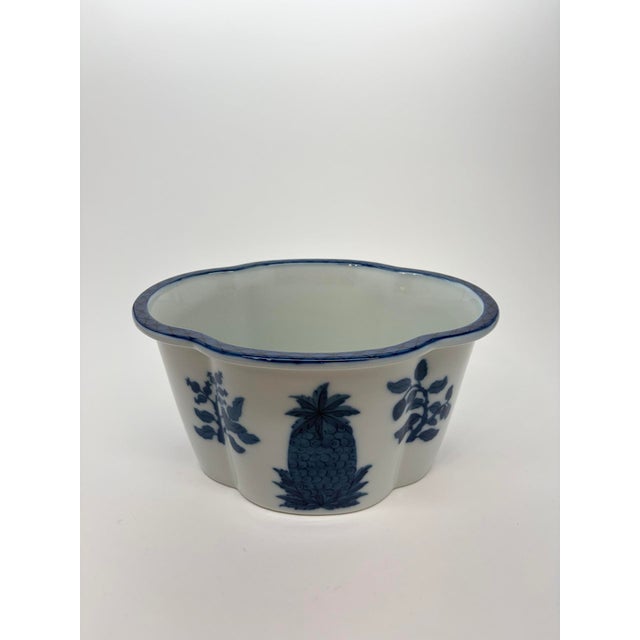 A vintage porcelain cachepot styled after Mottahedeh, with blue pineapple and leafy botanical decoration against a white...