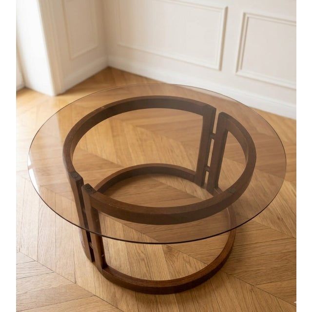 A stylish vintage round coffee table from the 1970s, featuring a smoked glass top and a sculptural wooden base with a...