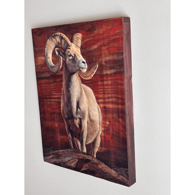 This oil painting on wood presents a majestic ram, poised confidently against a rich, textured background that echoes the...