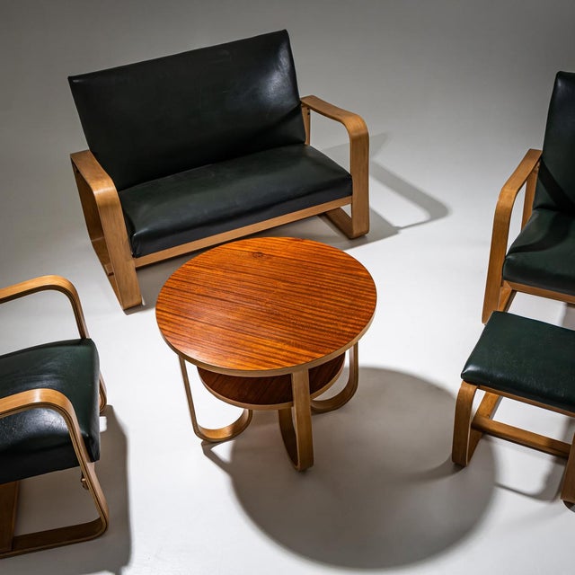 Seating ensemble comprising two armchairs, a two-seater sofa, a stool, and a side table. The pieces are upholstered in...
