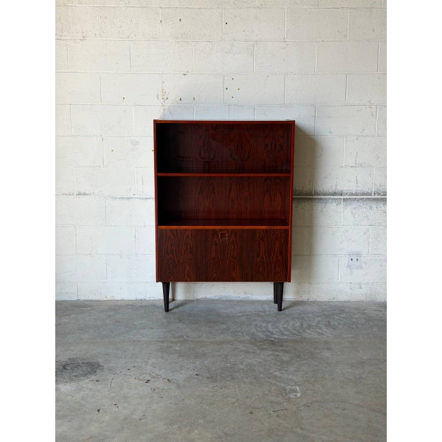 This striking storage unit features upper open shelves and a concealed lower compartment. Elevated on slender tapered...