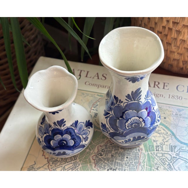 1980's Delft blue and white vase pair decorated in a floral design. Rounded with flared opening. Marked Delft with artist...