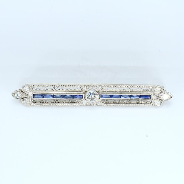 This elongated brooch features a central row of deep blue sapphires, flanked by intricate metalwork. A prominent round...