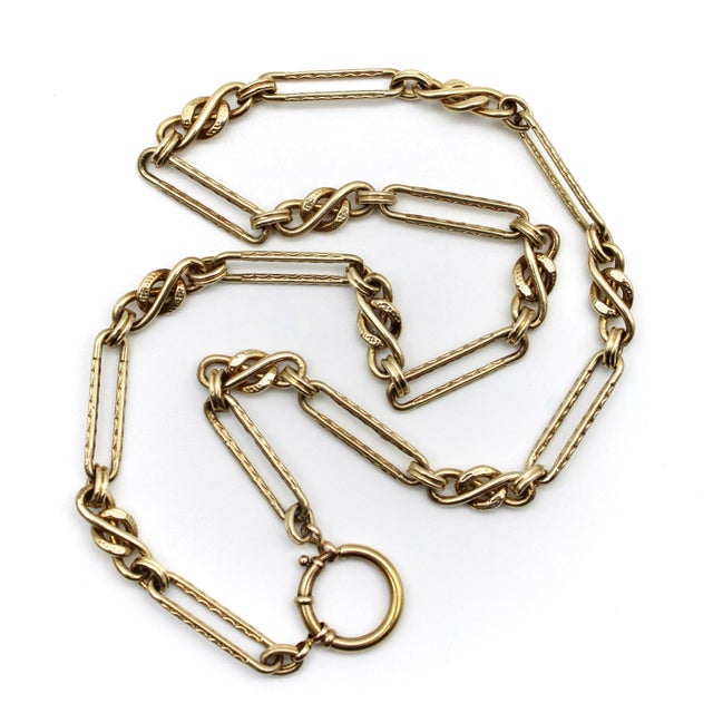 This 14k gold chain features an elongated paperclip link, alternated with a fettered knot that folds itself into an...