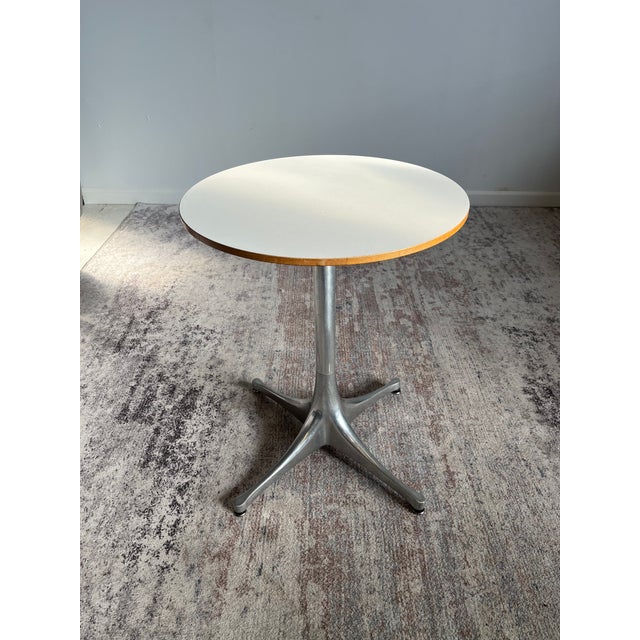 Designed by George Nelson for Herman Miller, this pedestal side table features a white laminate top on a cast aluminum...