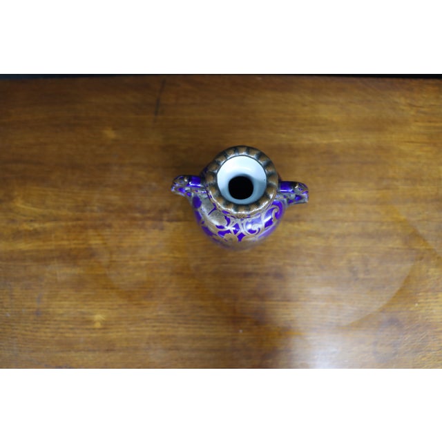 Cobalt blue glass vase featuring ornate copper-colored floral and scrolling vine decoration. The vase has an elongated...
