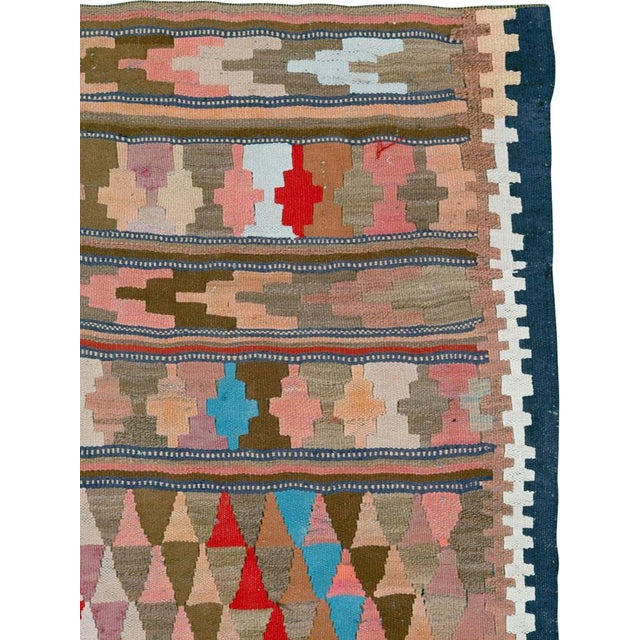 This Mid-20th century Persian flatweave kilim features a softly structured composition of horizontal bands filled with...