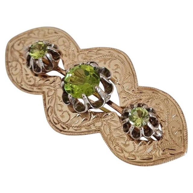 An elegant antique British brooch crafted in 9-carat yellow and white gold and claw-set with a series of vibrant green...