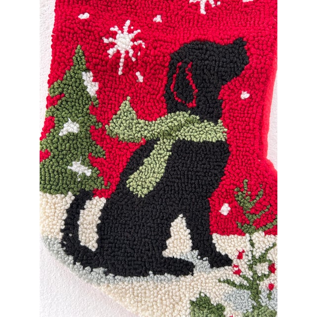 Offering a whimsical, hand hooked Christmas stocking featuring a black dog with scarf, trees and snow. The word "WOOF" is...