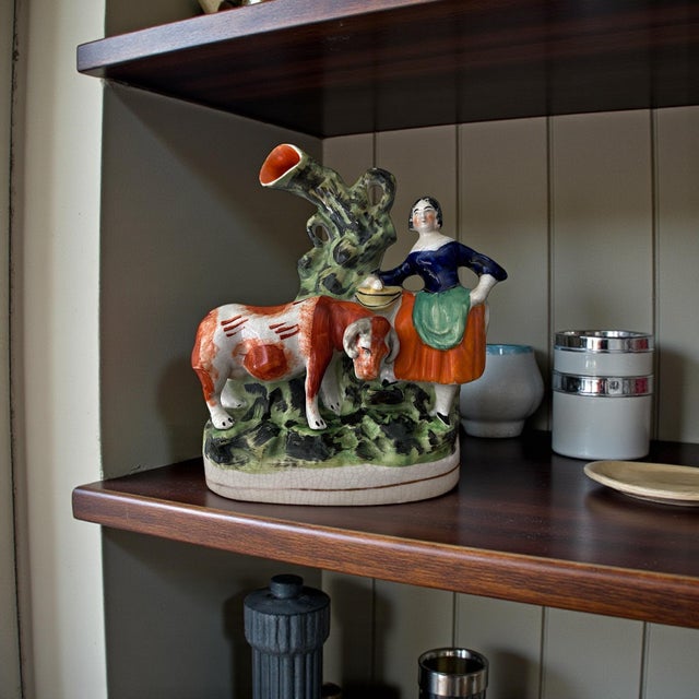 A finely modeled antique English Staffordshire figure depicting a pastoral scene of a woman and her cow beside a stylized...