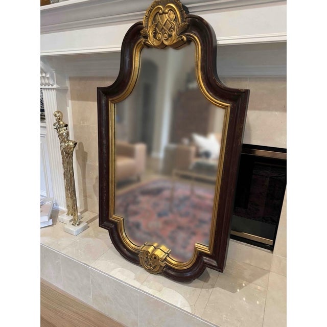 Large decorative wall mirror featuring a rich dark mahogany finish with antiqued gold accents and elegant carved details....