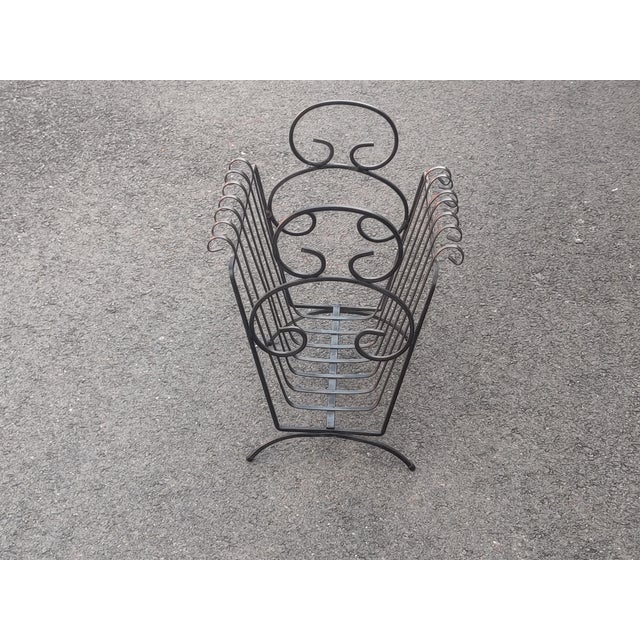 This is a vintage black wrought iron magazine rack or newspaper stand with beautiful, detailed scroll-work in the style of...