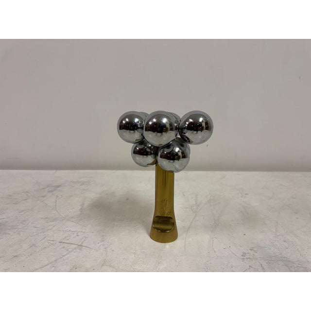 A bold and sculptural metal composition, combining polished chrome spheres with a warm brass support in a striking,...