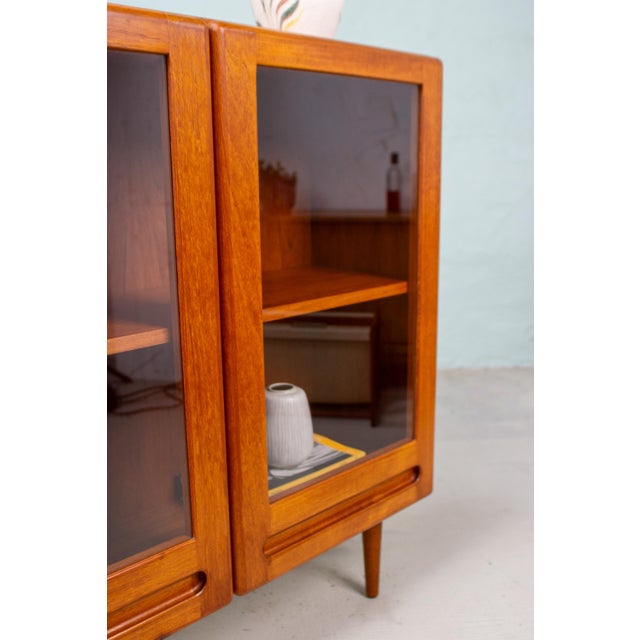 A teak display cabinet with a calm, clean aesthetic and a form that is pleasantly understated yet immediately eye-...