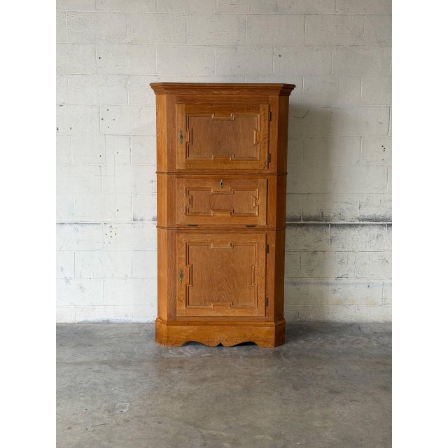 This corner storage cabinet features a triangular profile with three compartments. The facade is detailed with carved...