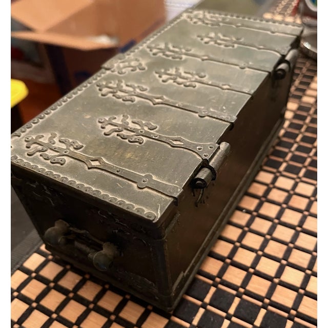 An antique small cast bronze lidded casket or strongbox with a wood-lined interior, decorative iron strap-work, side ring...