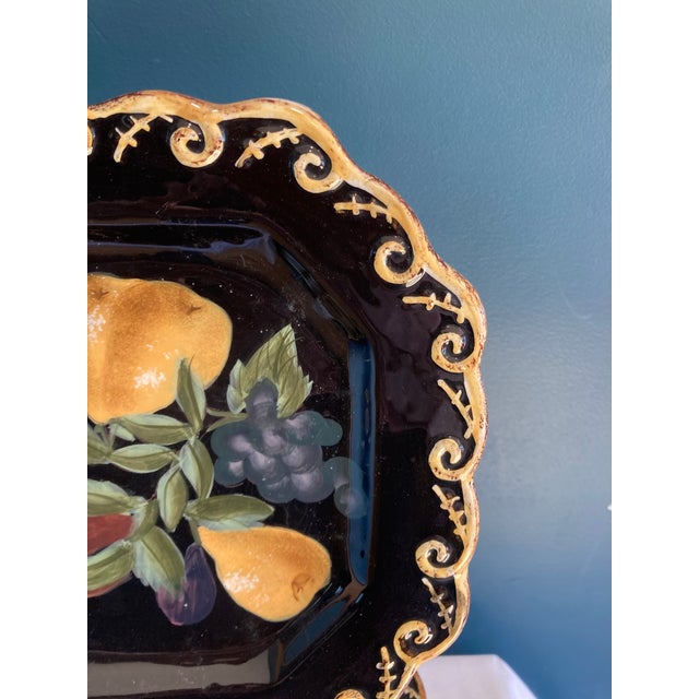 This set of six Raymond Waites plates showcases a bold black finish paired with hand-painted fruit imagery and ornate gold...