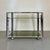 Elegant Space Age bar cart featuring a geometric chrome-plated metal frame and three shelves in olive-green smoked glass....