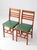 A pair of vintage 1950s folding chairs featuring warm reddish wood frames, slatted ladder backs, and green upholstered...