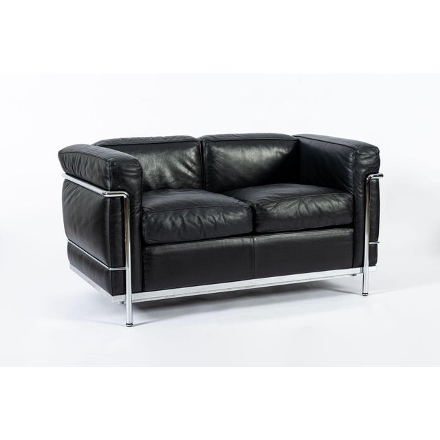 This authentic LC2 Petit Modele two-seat black leather sofa originally designed by Le Corbusier, Charlotte Perriand and...