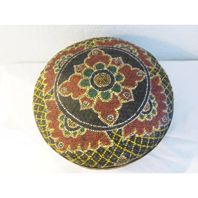 Colorful lidded decorative storage basket in woven, black rattan featuring a dot-art hand-painted design on exterior of...