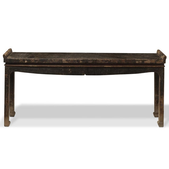 This narrow altar table from Qinghai, around the 1920s, features everted ends and a faded black lacquer finish with a...