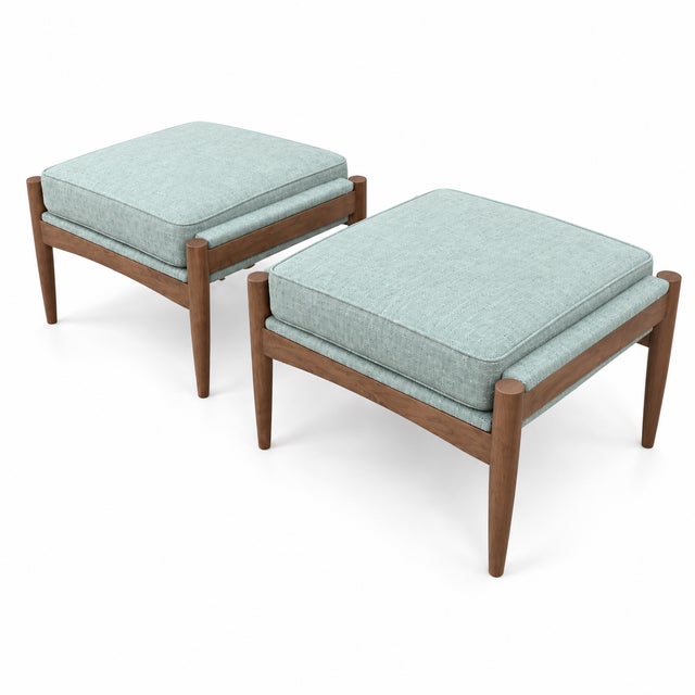 An elegant pair of ottomans featuring warm walnut bases and softly textured seafoam green chenille upholstery. Each frame...