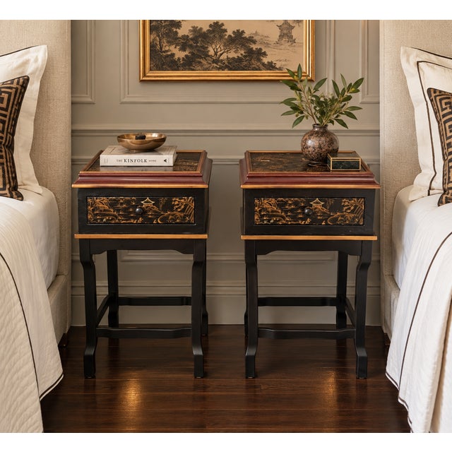 A charming pair of Chinoiserie-style nightstands featuring richly decorative Asian landscape scenes in warm gilt and...