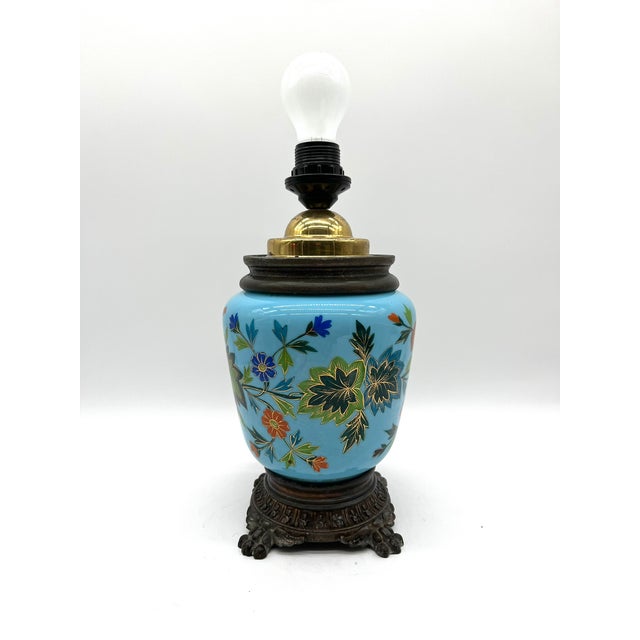 This distinctive table lamp from around 1890 combines colorful, hand-painted glass with elaborate cast brass in the...